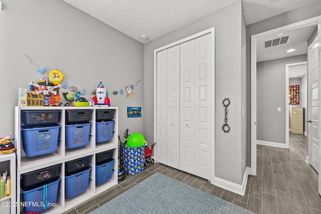 rec room featuring wood tiled floor, a textured ceiling, visible vents, and baseboards