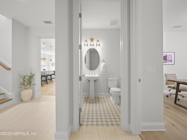 bathroom with visible vents, toilet, a sink, wood finished floors, and baseboards