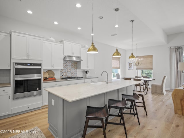 kitchen featuring stainless steel double oven, under cabinet range hood, a sink, gas stovetop, and backsplash