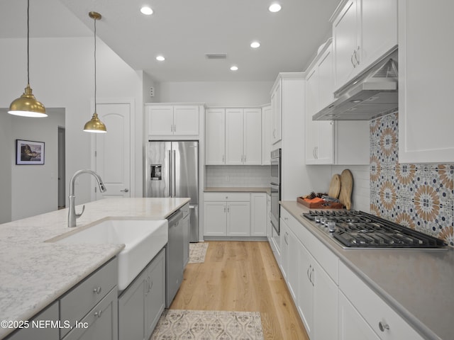 kitchen featuring under cabinet range hood, stainless steel appliances, a sink, white cabinets, and light wood finished floors