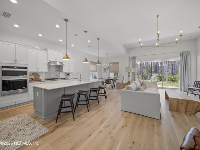 kitchen featuring double oven, a sink, visible vents, open floor plan, and an inviting chandelier