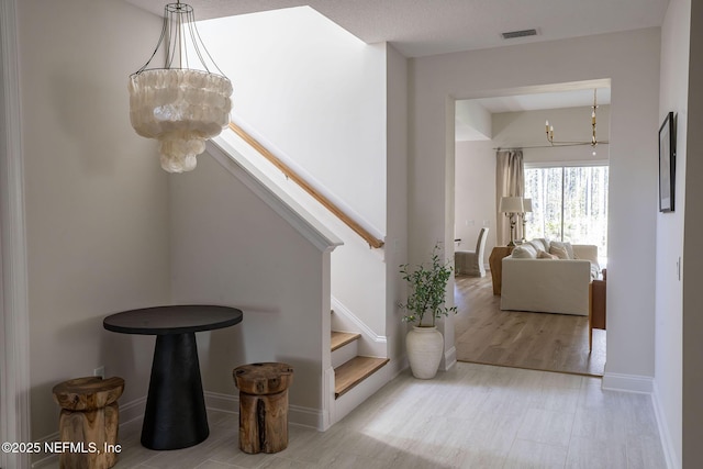 hall featuring visible vents, stairway, an inviting chandelier, wood finished floors, and baseboards