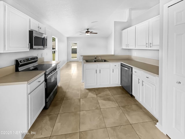 kitchen featuring light tile patterned floors, a peninsula, a sink, a ceiling fan, and appliances with stainless steel finishes