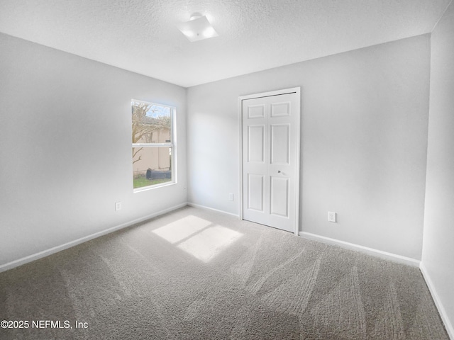 empty room featuring a textured ceiling, carpet floors, and baseboards