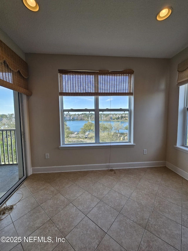 unfurnished room featuring a water view, tile patterned flooring, and baseboards