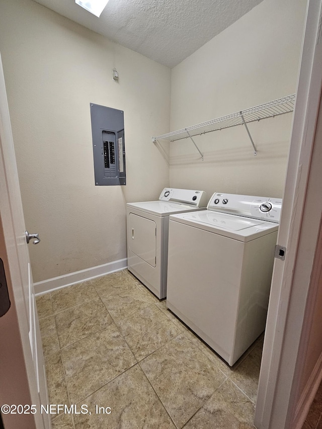 washroom featuring a textured ceiling, laundry area, baseboards, washer and dryer, and electric panel