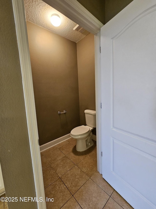 bathroom featuring a textured ceiling, toilet, visible vents, baseboards, and tile patterned floors