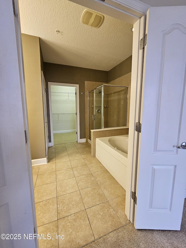 bathroom with a textured ceiling, a spacious closet, a shower stall, a bath, and tile patterned floors