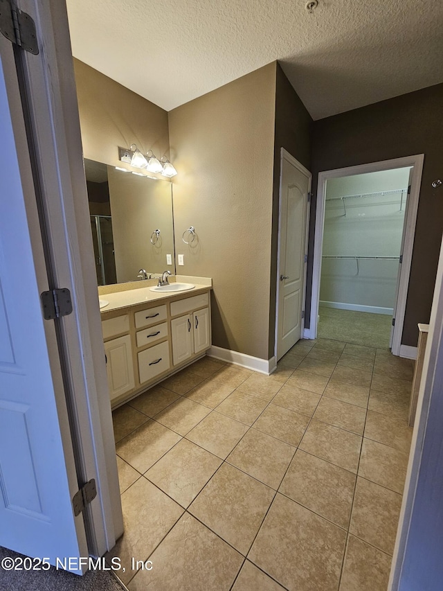 full bathroom with baseboards, tile patterned flooring, a spacious closet, a textured ceiling, and vanity