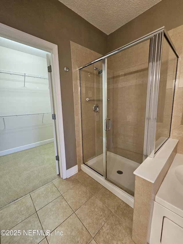 full bathroom with a textured ceiling, tile patterned flooring, baseboards, a spacious closet, and a shower stall