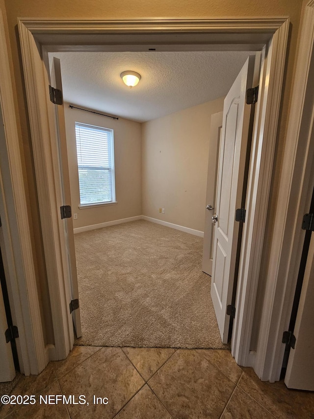 unfurnished bedroom with carpet flooring, a textured ceiling, and baseboards