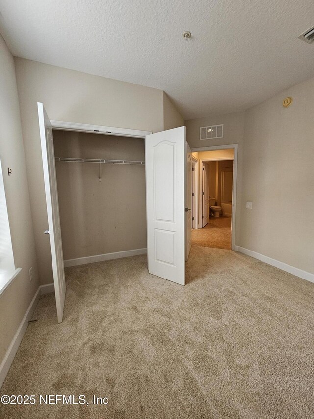 unfurnished bedroom featuring carpet floors, a textured ceiling, visible vents, and a closet