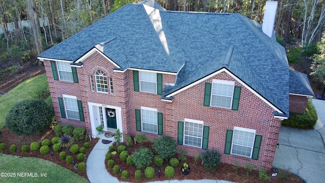 colonial house featuring brick siding, a chimney, and a shingled roof