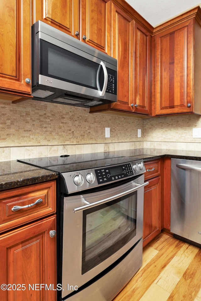 kitchen featuring appliances with stainless steel finishes, light wood finished floors, dark stone countertops, and tasteful backsplash