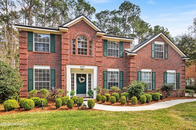 colonial inspired home with brick siding and a front yard