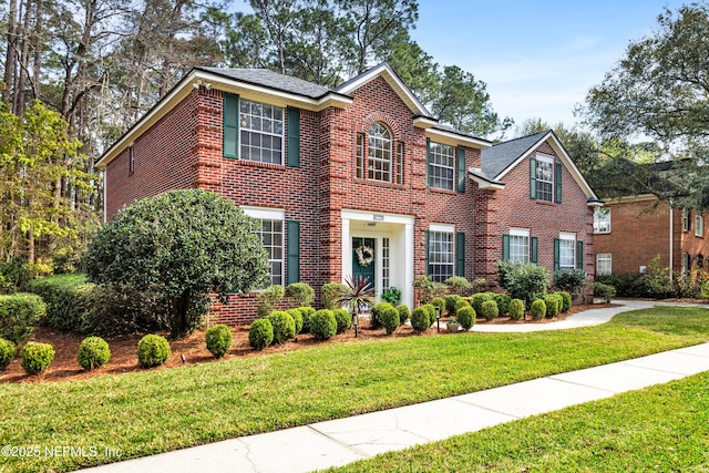 colonial-style house featuring brick siding and a front yard