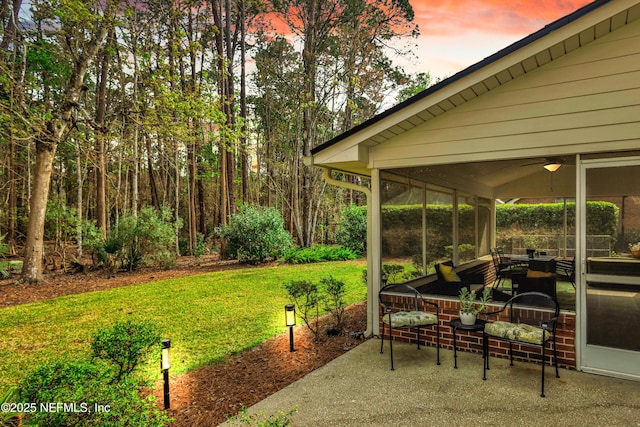 patio terrace at dusk featuring a sunroom and a lawn