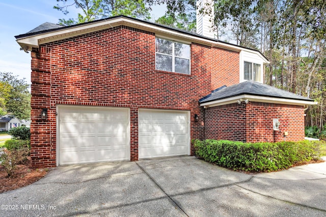 view of side of home with driveway, an attached garage, a chimney, and brick siding