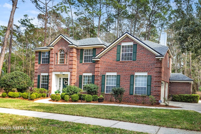 colonial house featuring a chimney, a front lawn, and brick siding