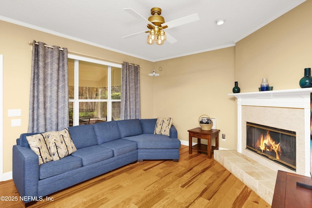 living area with baseboards, a tiled fireplace, wood finished floors, and crown molding