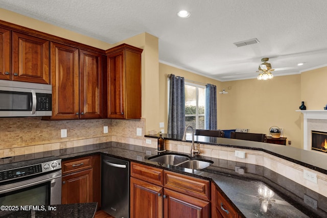 kitchen featuring a sink, visible vents, appliances with stainless steel finishes, backsplash, and a glass covered fireplace