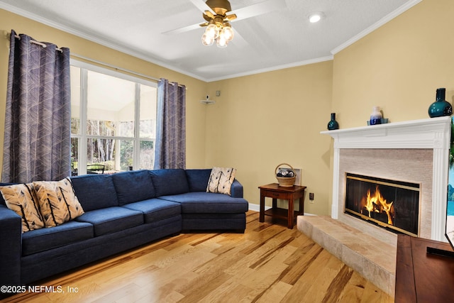 living area with baseboards, a tile fireplace, light wood-style flooring, ceiling fan, and crown molding