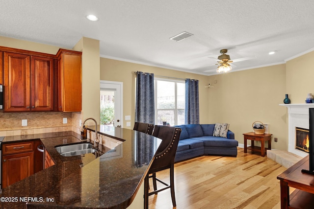 kitchen with a peninsula, a sink, open floor plan, light wood-type flooring, and a glass covered fireplace