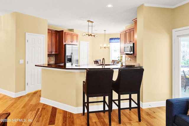 kitchen with dark countertops, light wood-style flooring, a peninsula, an inviting chandelier, and stainless steel appliances