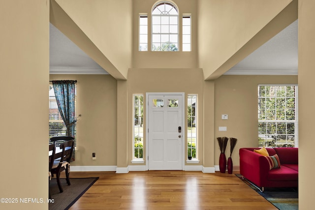 foyer with baseboards, a high ceiling, wood finished floors, and crown molding