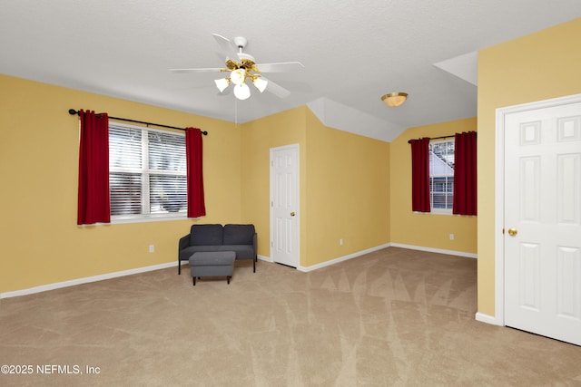 unfurnished room featuring a textured ceiling, lofted ceiling, light carpet, a ceiling fan, and baseboards