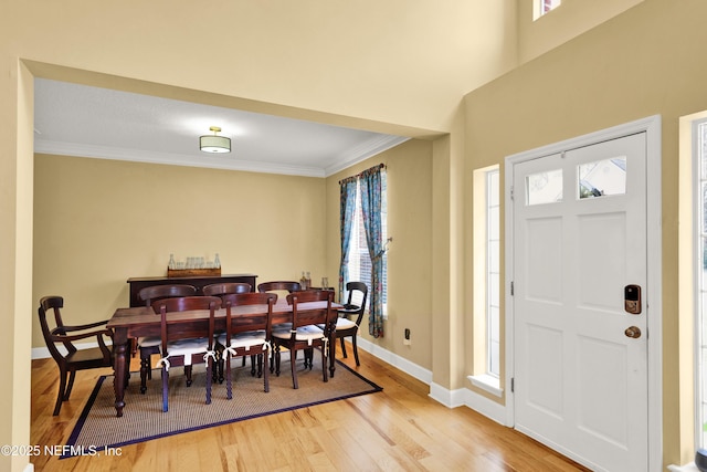 dining room with a wealth of natural light, baseboards, crown molding, and light wood finished floors