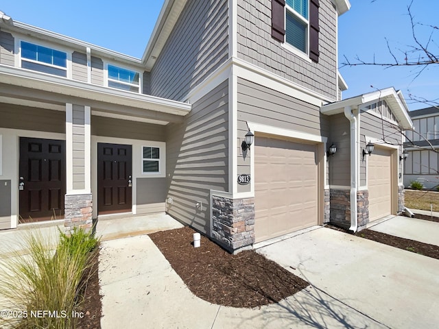 property entrance with a garage, stone siding, and driveway