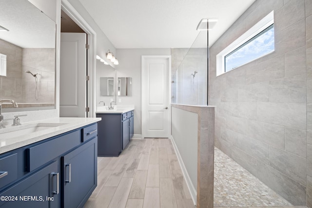 bathroom featuring wood finish floors, a sink, two vanities, baseboards, and walk in shower