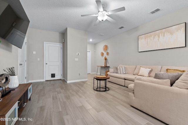 living room featuring visible vents, a textured ceiling, light wood-type flooring, and baseboards