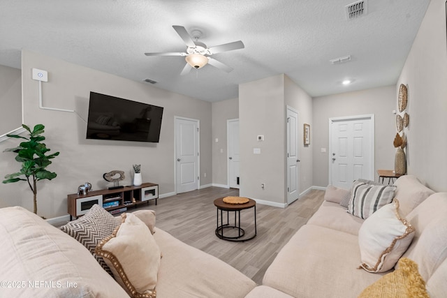 living room with a ceiling fan, visible vents, light wood finished floors, and a textured ceiling