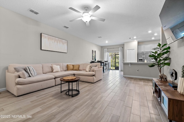 living room with light wood finished floors, visible vents, a textured ceiling, and a ceiling fan