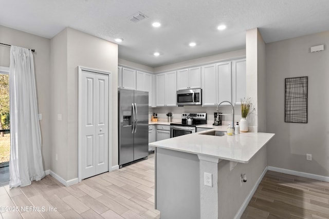 kitchen with wood finish floors, light countertops, appliances with stainless steel finishes, a peninsula, and a sink