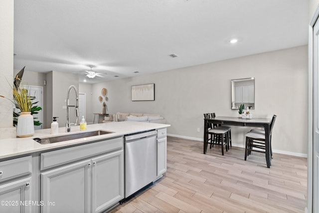 kitchen featuring dishwasher, light countertops, light wood-style flooring, a ceiling fan, and a sink