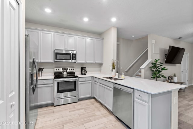 kitchen featuring wood finish floors, a sink, stainless steel appliances, a peninsula, and light countertops