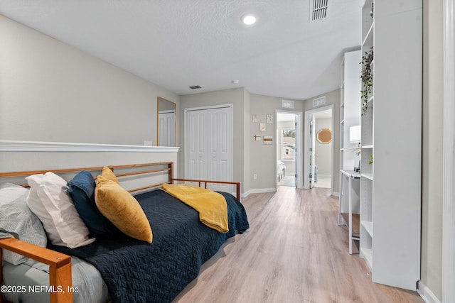 bedroom featuring visible vents, baseboards, light wood-type flooring, a closet, and a textured ceiling