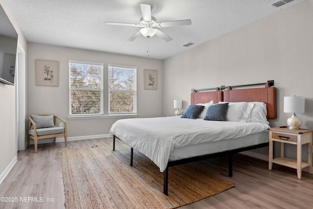 bedroom with visible vents, baseboards, a textured ceiling, and wood finished floors