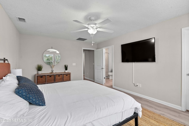 bedroom with visible vents, a textured ceiling, baseboards, and wood finished floors