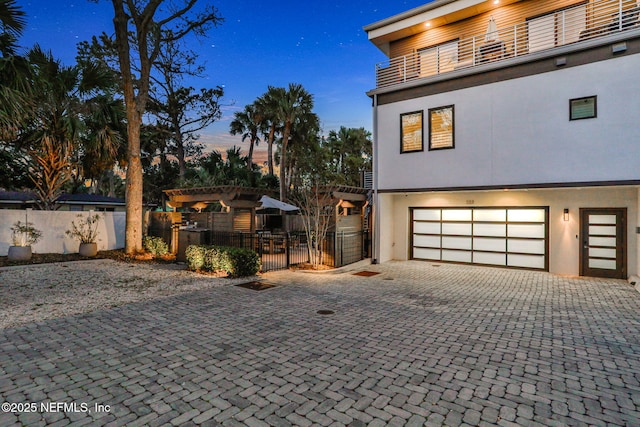 view of front facade featuring a balcony, fence, decorative driveway, and stucco siding