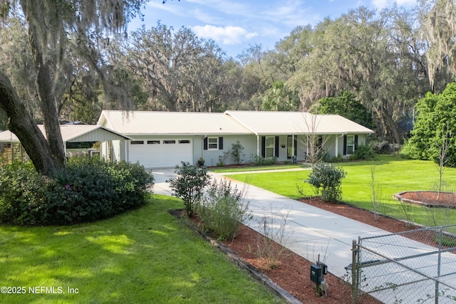 ranch-style home with a front yard, concrete driveway, metal roof, and an attached garage