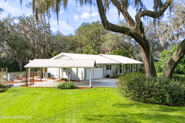 rear view of property featuring metal roof, an attached garage, central air condition unit, concrete driveway, and a lawn