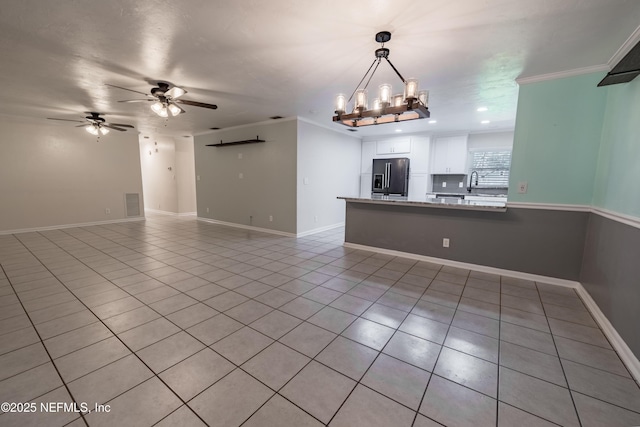 interior space with light tile patterned floors, baseboards, ornamental molding, a sink, and ceiling fan with notable chandelier