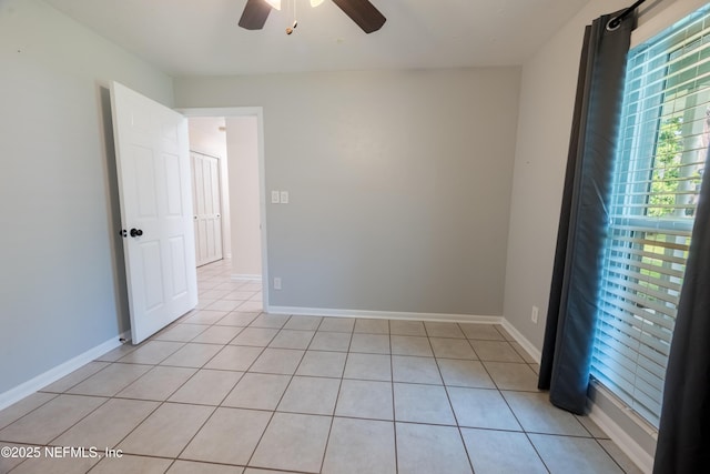 empty room with light tile patterned floors, ceiling fan, and baseboards