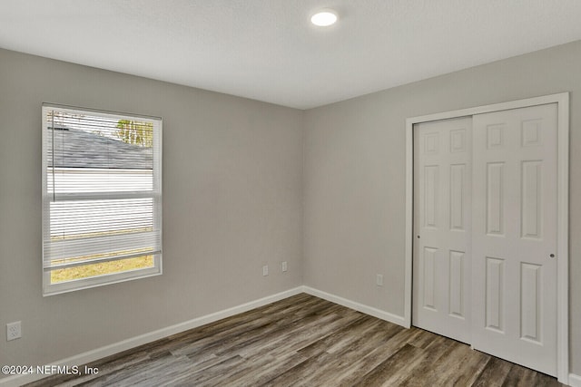 unfurnished bedroom featuring a closet, multiple windows, baseboards, and wood finished floors