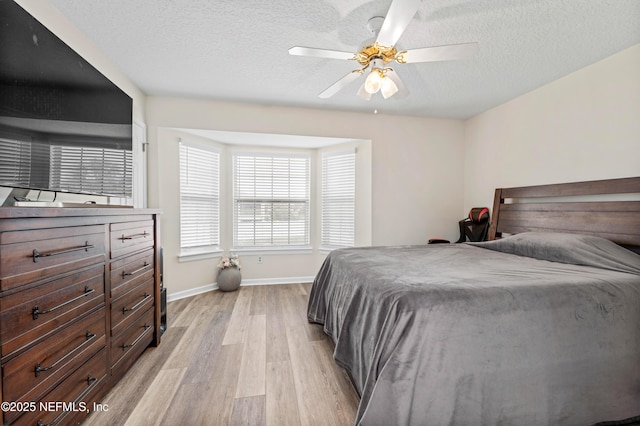 bedroom with light wood-style floors, a textured ceiling, baseboards, and a ceiling fan