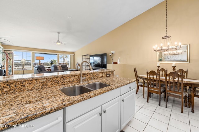 kitchen with light stone counters, light tile patterned flooring, a sink, white cabinets, and vaulted ceiling